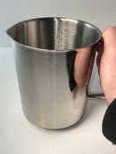 Metal pitcher held by a hand on a light gray background
